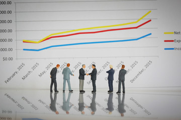 Selective focus of miniature businessman handshake and line chart background as business, commitment, partnership and investment concept.