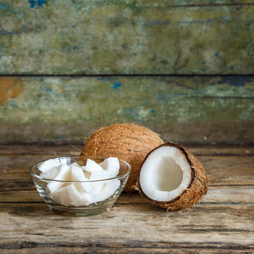 Fresh whole and cut in half coconuts with coconut shreds on wooden background with copy space