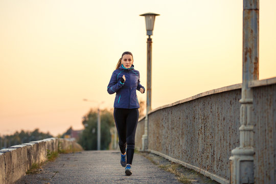 Young sporty woman jogging on bridge in the morning. Running fitness girl in sportswear outdoor image with copy space