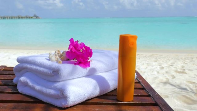 Male hand put Skin Care lotion on the sunbed. Sunscreen on Maldives beach. Sunblock on the sunbed and sea background in Maldives.Sun lotion, white hotel towels and tropical flowers with sea background