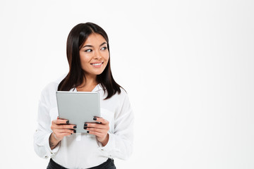 Cheerful young asian lady chatting by tablet computer. Looking aside.