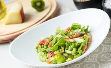 A delicious salad with salmon, lettuce, kiwi, pine nuts, Parmesan cheese. Close-up