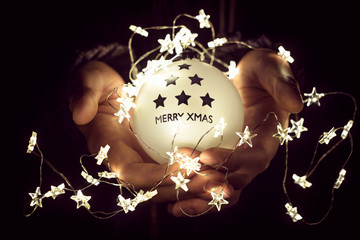 Christmas ball with the word merry xmas in man's hands. Christmas lights - 179746307