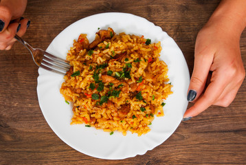 woman hand holding fork with Rice with Vegetables and Meat in a plate on wooden table. top view.