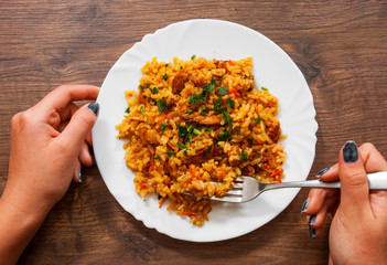 woman hand holding fork with Rice with Vegetables and Meat in a plate on wooden table. top view.