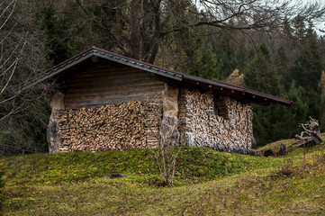Holzhütte im Garten mit gespaltenem Brennholz in den Alpen