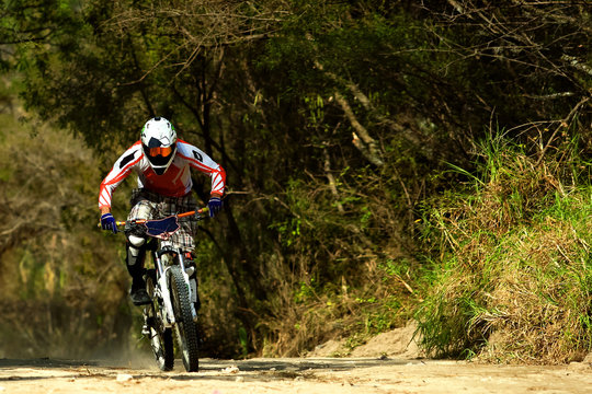 Downhill mountain biker wearing a white orange costume riding at fast speed down hill