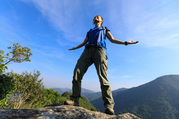 successful young woman backpacker breathing fresh air at cliff's edge on top of mountain