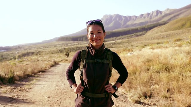 Video of woman with backpack standing in countryside and smiling. Asian female hiker in nature looking at camera and smiling.