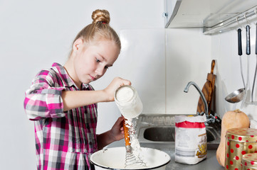 Young beautiful smiling girl breaks an egg into deep dish. Cute blonde cooking in a home kitchen