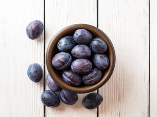 Fresh plums in ceramic bowl on white wooden background.