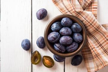 Fresh plums in ceramic bowl on white wooden background.