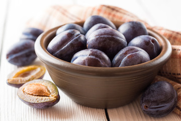 Fresh plums in ceramic bowl on white wooden background.