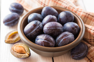 Fresh plums in ceramic bowl on white wooden background.