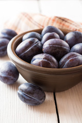 Fresh plums in ceramic bowl on white wooden background.
