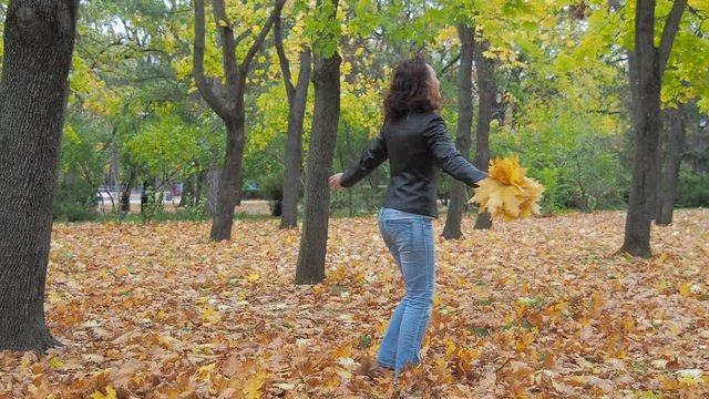 A happy woman is walking on yellow leaves in an autumn park.