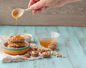 Oatmeal cookies with nuts, sesame and honey on a wooden background. Female hands. Menu for a bakery, cafe