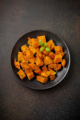 Fried pumpkin slices with herbs and pepper, olive oil in a black ceramic plate on  dark concrete or stone background. Selective focus. Top view.