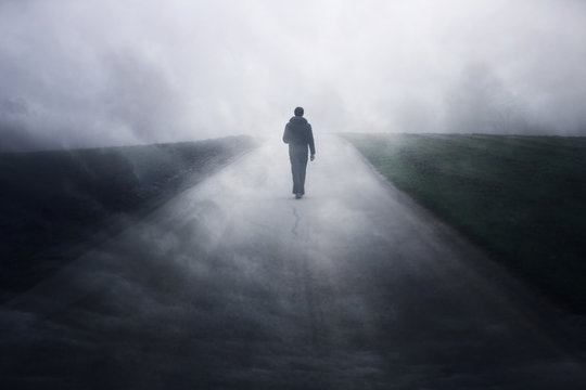 Man Walking Alone On Dark Misty Foggy Asphalt Road. 