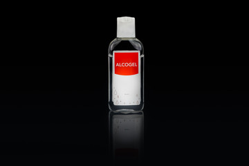 Isolated alcogel hand disinfectant in a small plastic bottle with red label, studio shot on black background.
