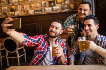 Cheerful friends having fun taking selfie and drinking draft beer in pub.