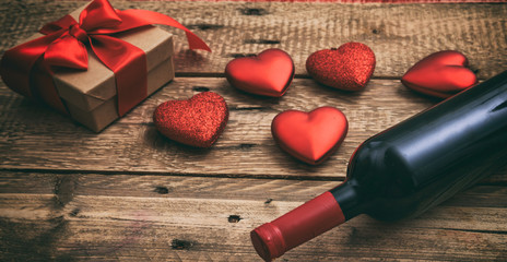 Valentines day. Red wine bottle, a gift and hearts on wooden background