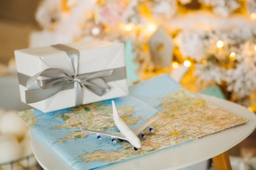 Naklejka na ściany i meble Travel present for New Year. Toy airplane with map, present box and Christmas tree. Cozy lights decoration. Happy Xmas!