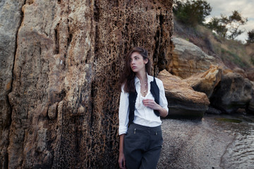 business woman on suit vest and white shirt standing near big stone on the sea cost