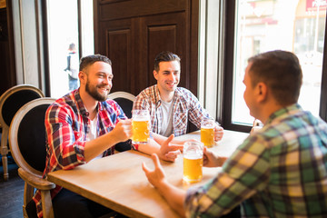 Cheerful friends having fun and drinking draft beer in pub.