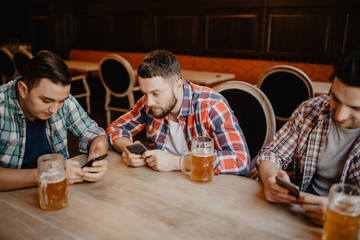 male friends with smartphones addicted drinking beer at bar or pub
