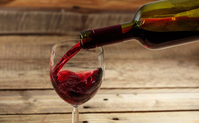 Pouring red wine in a glass on wooden background