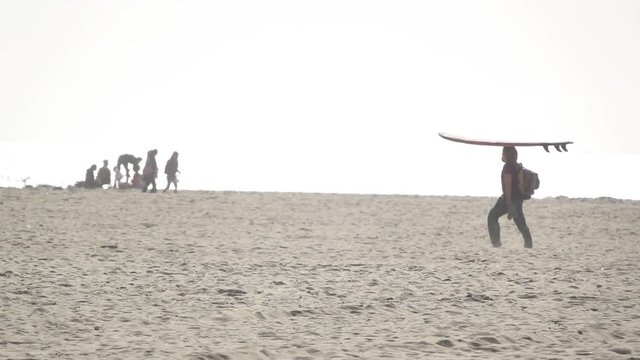 Man walks along beach, carrying surfboard on his head