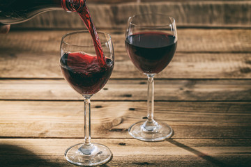 Pouring red wine in a glass on wooden background
