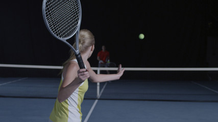Woman stands ready to hit a tennis ball on court at night