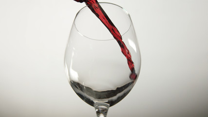 Obraz na płótnie Canvas Red wine begins to pour into an empty wine glass