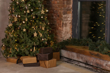 Christmas tree with wooden rustic decorations and presents under it in dark loft interior.