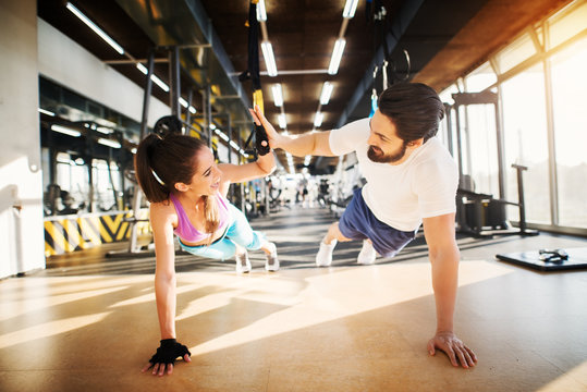 Young beautiful fitness couple smiling and clapping hands each other while doing push ups together in the gym.