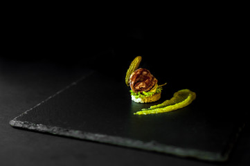 canapés with marinated cucumber, mustard and salami. black background and slate.