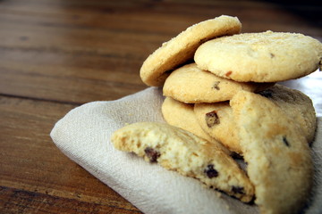 Selection of choc chip and fruit cookies, on a serSelection of choc chip and fruit cookies, on a serviette on a wooden table. Copy space for textviette on a wooden table