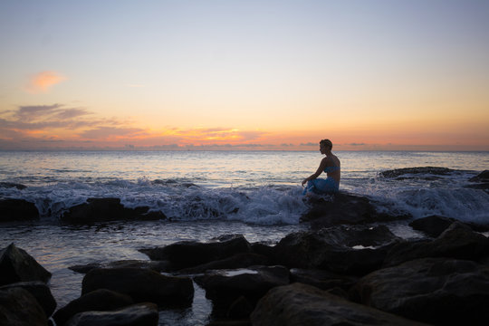 Thoughtful woman sitting on rock at beach during sunset