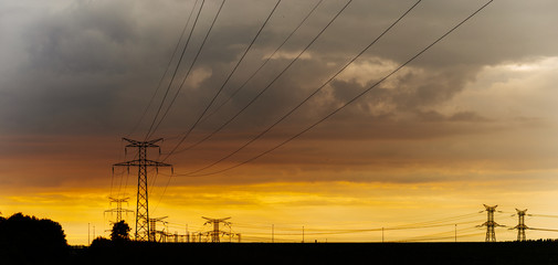High voltage power lines and transmission towers at sunset. Poles and overhead power lines silhouettes in the dusk. Electricity generation and distribution. Electric power industry and nature concept