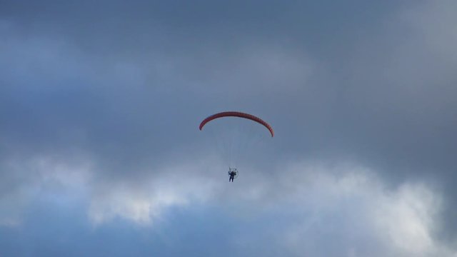 Daring paraglider flying high in the storm clouds. Air sport and recreation. A powered paraglider - a glider with a dorsal power plant, providing the rise and moving in the air.  
