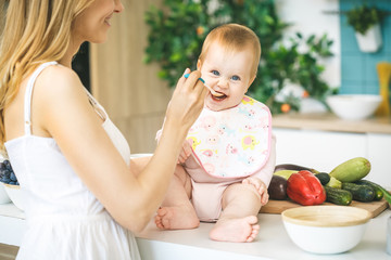 Mother Feeding Her Baby Girl with a Spoon. Mother Giving Food to her adorable Child at Home. Baby food