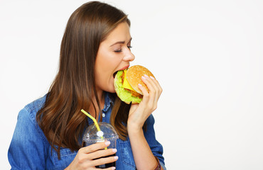 Woman with closed eyes biting burger holding cola drink in glass.