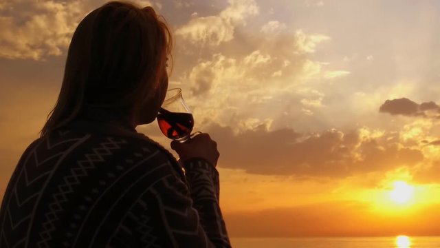 girl sitting on the beach looking at the sunset and drinking mulled wine