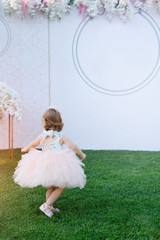 The back side of a little girl in a dress that runs across the lawn on the background of a white banner.