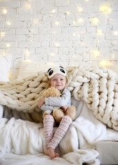 Young baby girl sitting dreaming near magical New year craft gifts by a Christmas tree