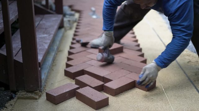 Using a rubber mallet, a hardscaper taps the red brick pavers into place.