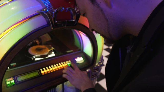 Man trying to choose good song on old jukebox dropping coin and pushing keys