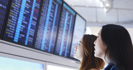 Obraz premium Girl friends checking time schedule on mobile phone in Hong Kong airport